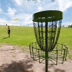 Student throwing a disc at a disc golf basket on the Michigan Tech course.